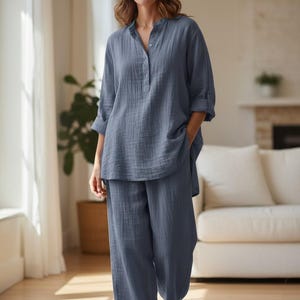 Puede incluir: Un conjunto de descanso de dos piezas en color azul polvoriento, compuesto por una camisa de manga larga con cuello mao y botones, y un pantalón ancho a juego. La tela presenta una textura arrugada visible y las mangas están remangadas.