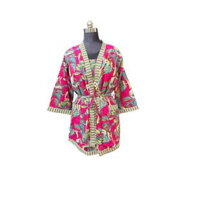 May include: A short, pink robe with a tropical print of monkeys and leaves. The robe has a matching belt and green and white striped trim on the edges and sleeves. The robe is displayed on a mannequin.