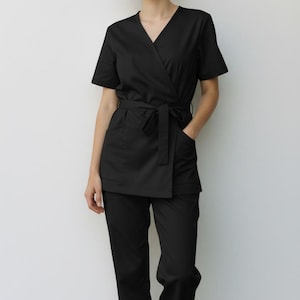 May include: Black wrap-style medical scrubs with a V-neck top and matching pants. The top has short sleeves and a tie belt at the waist. The pants are straight-legged. The outfit is made of a soft, wrinkle-resistant fabric.