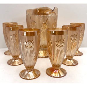 May include: A vintage amber glass pitcher and matching glasses set. The pitcher and glasses feature a floral design and vertical ribbed detailing. The set includes a pitcher and six stemmed glasses, perfect for serving beverages.