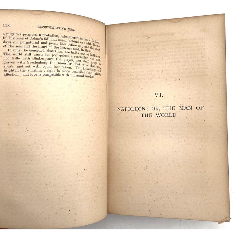 May include: An open book with aged, off-white pages. The left page has text about a pilgrim's progress and the right page reads "NAPOLEON; OR, THE MAN OF THE WORLD." The book is from the "REPRESENTATIVE MEN" series.