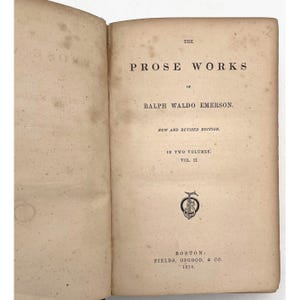 May include: An open book with aged, off-white pages. The text reads "THE PROSE WORKS of RALPH WALDO EMERSON. NEW AND REVISED EDITION. IN TWO VOLUMES. VOL. II." Published in Boston by FIELDS, OSGOOD, & CO. in 1870. Includes a decorative emblem.