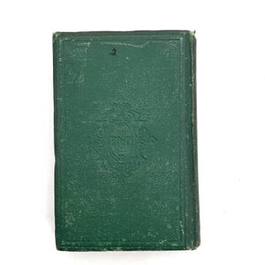 May include: A vintage book with a dark green cover. The cover has an embossed decorative design and the number "2" in the upper corner. The book's edges show signs of wear, indicating its age and use. The book is likely a collectible.