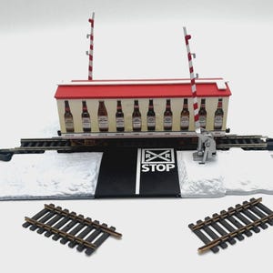 May include: A model train set with a red and white train car with a red roof and a white 'RR STOP' sign. The train car is decorated with a row of beer bottles. The train set includes two sets of tracks and two red and white crossing gates.