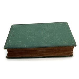 May include: A vintage, hardcover book with a distressed green cover. The cover has an embossed design and shows signs of wear. The pages have a warm, aged tone. The book is lying flat, showcasing its rectangular shape and aged appearance.