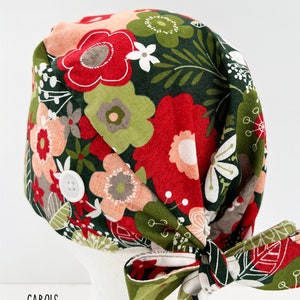 May include: A floral patterned scrub cap with a bow. The cap features a dark green background with red, pink, and white flowers. A white button is on the side. The word "CAROLS" is printed at the bottom.