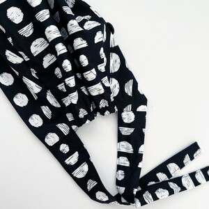 May include: Black and white patterned fabric scrub cap with two long ties. The fabric has a geometric pattern of circles and semi-circles.