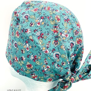 K&ouml;nnte beinhalten: Eine tealblaue OP-M&uuml;tze mit einem floralen Muster in Rot-, Gelb- und Wei&szlig;t&ouml;nen. Die M&uuml;tze hat einen Bindfaden an der R&uuml;ckseite.