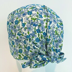 K&ouml;nnte beinhalten: Eine wei&szlig;e OP-M&uuml;tze mit einem blauen und gr&uuml;nen Blumenmuster. Die M&uuml;tze hat einen Knoten am R&uuml;cken.