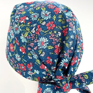 K&ouml;nnte beinhalten: Eine blaue OP-M&uuml;tze mit einem Blumenmuster mit rosa, roten und wei&szlig;en Bl&uuml;ten. Die M&uuml;tze hat einen Knoten am Hinterkopf.