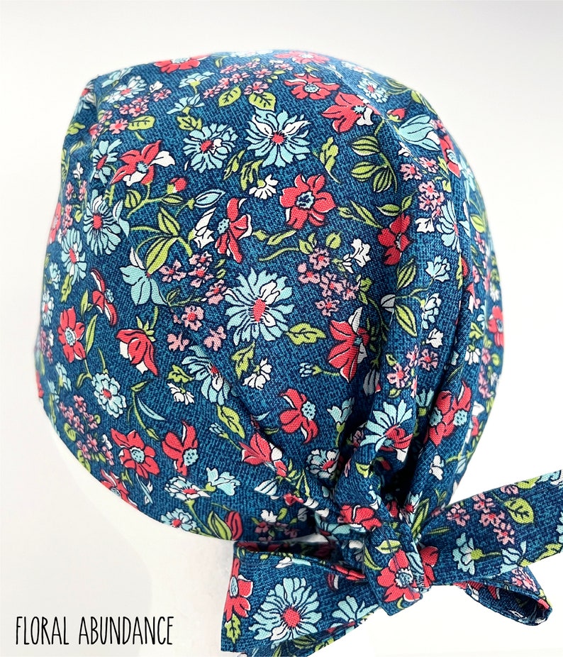 K&ouml;nnte beinhalten: Eine blaue OP-M&uuml;tze mit einem Blumenmuster mit rosa, roten und wei&szlig;en Bl&uuml;ten. Die M&uuml;tze hat einen Knoten am Hinterkopf.