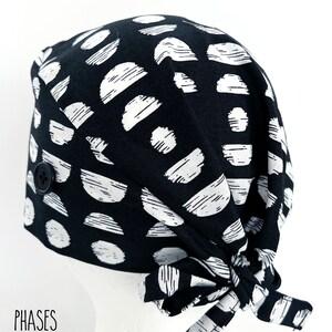 May include: Black and white patterned surgical scrub hat with a button closure. The hat has a tie at the back.