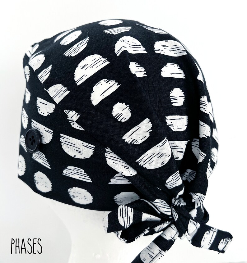 May include: Black and white patterned surgical scrub hat with a button closure. The hat has a tie at the back.