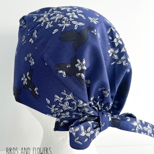 K&ouml;nnte beinhalten: Eine blaue OP-M&uuml;tze mit einem wei&szlig;en und schwarzen Blumenmuster. Die M&uuml;tze ist hinten mit einer Schleife gebunden.