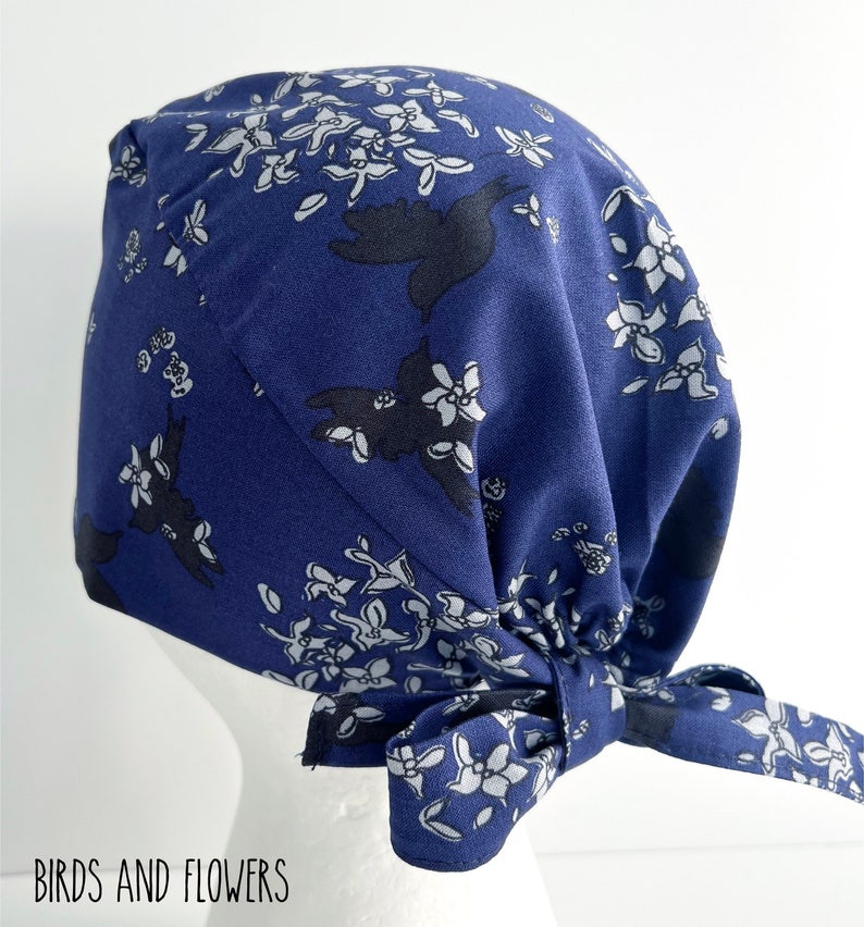 K&ouml;nnte beinhalten: Eine blaue OP-M&uuml;tze mit einem wei&szlig;en und schwarzen Blumenmuster. Die M&uuml;tze ist hinten mit einer Schleife gebunden.