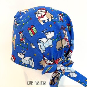 May include: A blue surgical scrub cap featuring a festive Christmas dog pattern. The cap is adorned with various dog breeds dressed in holiday attire, including Santa hats and angel wings, along with Christmas lights and gift boxes. The text "CHRISTMAS DOGS" is printed on the bottom.