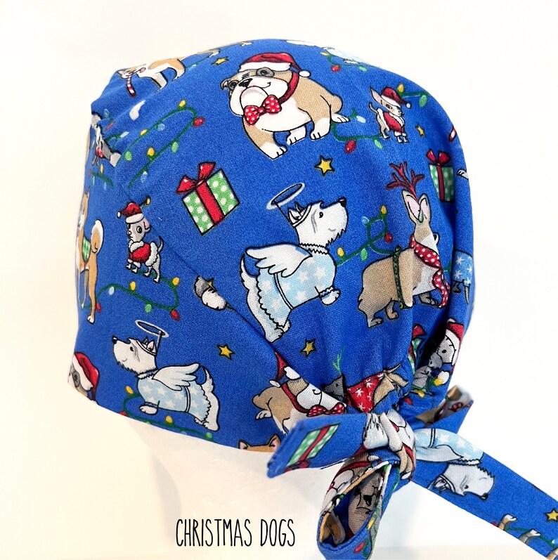 May include: A blue surgical scrub cap featuring a festive Christmas dog pattern. The cap is adorned with various dog breeds dressed in holiday attire, including Santa hats and angel wings, along with Christmas lights and gift boxes. The text "CHRISTMAS DOGS" is printed on the bottom.