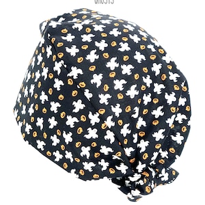 May include: Black fabric cap with a repeating pattern of white ghosts and orange jack-o'-lanterns. The word "GHOSTS" is printed in black at the top. This Halloween-themed cap is likely for medical professionals or those in the service industry.