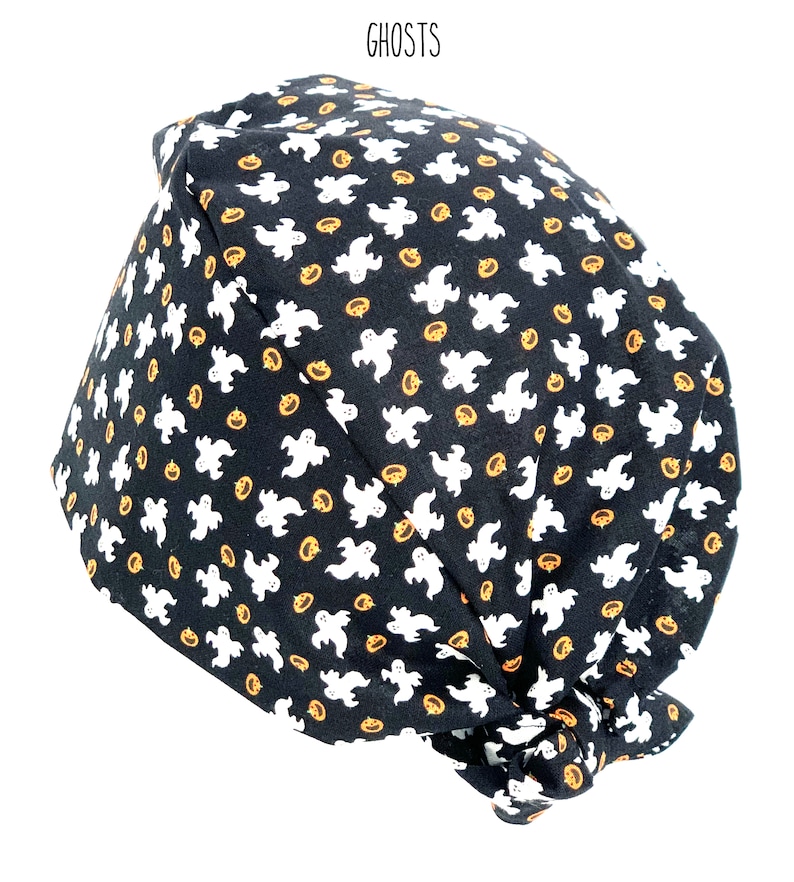 May include: Black fabric cap with a repeating pattern of white ghosts and orange jack-o'-lanterns. The word "GHOSTS" is printed in black at the top. This Halloween-themed cap is likely for medical professionals or those in the service industry.