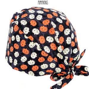 May include: A black surgical scrub cap with a repeating pattern of orange and white jack-o'-lanterns. The cap is tied at the back with matching fabric. The word "PUMPKINS" is printed at the top.
