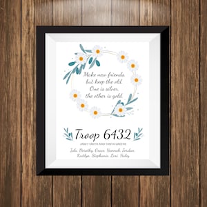 May include: A framed print with a white daisy wreath and a quote about friendship. The text reads "Make new friends, but keep the old. One is silver, the other is gold." Below the quote is "Troop 6432" and the names "Janet Smith and Tanya Greene" and "Isla, Dorothy, Grace, Hannah, Jordan, Kaitlyn, Stephanie, Lexi, Haley".