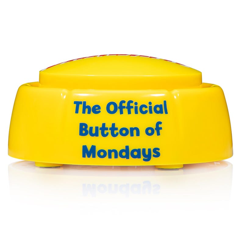 May include: A bright yellow plastic push button with a rounded top. The front of the button features the blue text "The Official Button of Mondays" printed in a clear, sans-serif font. The base is circular with a smooth, glossy finish.