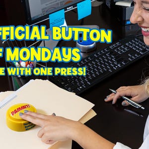 May include: A round yellow plastic button with the word DAMMIT! printed in red on the top surface. The button is resting on a stack of beige paper folders on a dark desk surface. The text THE OFFICIAL BUTTON OF MONDAYS SMILE WITH ONE PRESS! is visible.