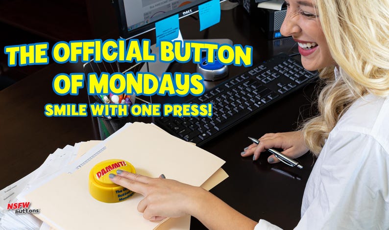 May include: A round yellow plastic button with the word DAMMIT! printed in red on the top surface. The button is resting on a stack of beige paper folders on a dark desk surface. The text THE OFFICIAL BUTTON OF MONDAYS SMILE WITH ONE PRESS! is visible.