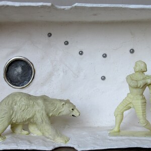 May include: A white polar bear figurine walks towards a white knight figurine holding a sword, both figures are set against a white background with a silver circle and a constellation of silver dots.