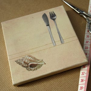 May include: A beige canvas with a seashell design and a silver knife and fork. The canvas is on a brown surface.