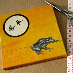 May include: A yellow canvas with a black circle containing a stylised heartbeat graphic. A black and white frog is cut out and glued to the canvas.