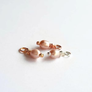May include: Three small, handcrafted jewelry clasps. Each clasp features a lustrous, peach-colored pearl bead, wire-wrapped with either gold, rose gold, or silver-colored wire. The clasps are designed for jewelry making.
