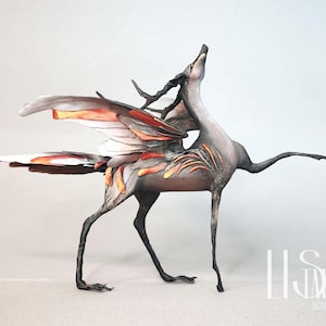 Puede incluir: Escultura de una criatura mítica con cuerpo de caballo, alas y cuernos. La criatura es principalmente gris con acentos naranjas y rojos en las alas y el cuerpo. La escultura está de pie con la cabeza levantada y un brazo extendido.