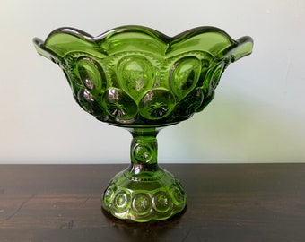 May include: A green glass bowl with a pedestal base. The bowl has a scalloped rim and is decorated with a repeating pattern of stars and moons.