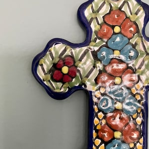 May include: A blue and white ceramic cross with a floral design. The cross is decorated with red, blue, and yellow flowers.