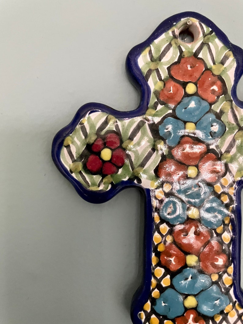 May include: A blue and white ceramic cross with a floral design. The cross is decorated with red, blue, and yellow flowers.