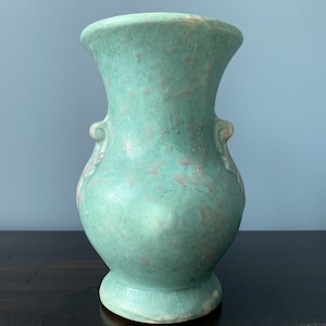May include: A vintage green ceramic vase with ornate handles. The vase has a mottled glaze and a slightly distressed look.