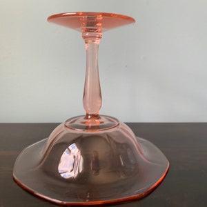 May include: A pink glass pedestal cake stand with a scalloped edge and a single stem.