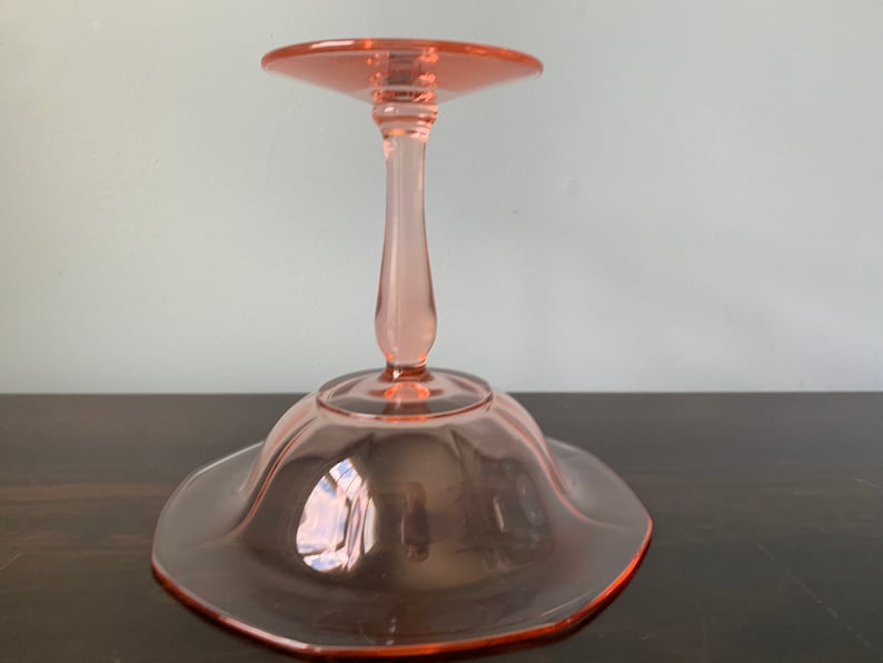 May include: A pink glass pedestal cake stand with a scalloped edge and a single stem.