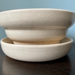May include: A set of two white ceramic bowls, one nested inside the other. The bowls have a slightly textured surface and a rounded shape.