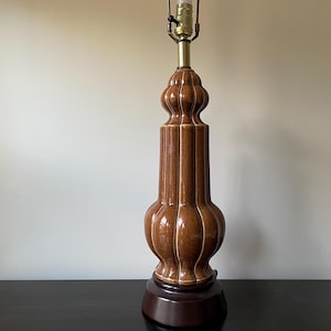 May include: A brown ceramic table lamp with a textured, ribbed design. The lamp has a round base and a bulbous, rounded body.