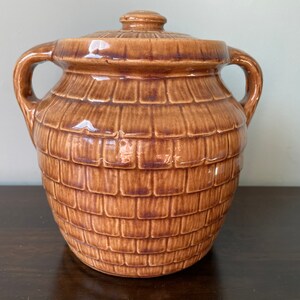 May include: A brown ceramic cookie jar with a lid and two handles. The jar is decorated with a basket weave pattern.