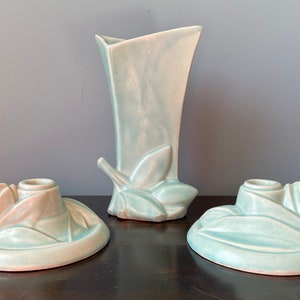 May include: A set of three vintage ceramic pieces in a light blue glaze. The set includes a vase and two candle holders. Each piece features a stylized leaf design.