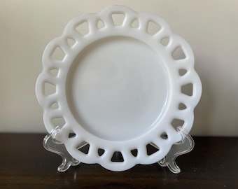 May include: White milk glass plate with a scalloped edge and a cut-out design. The plate is on a clear plastic stand.