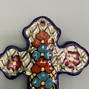 May include: A blue and white ceramic cross with a floral design. The cross is decorated with red, blue, and yellow flowers.