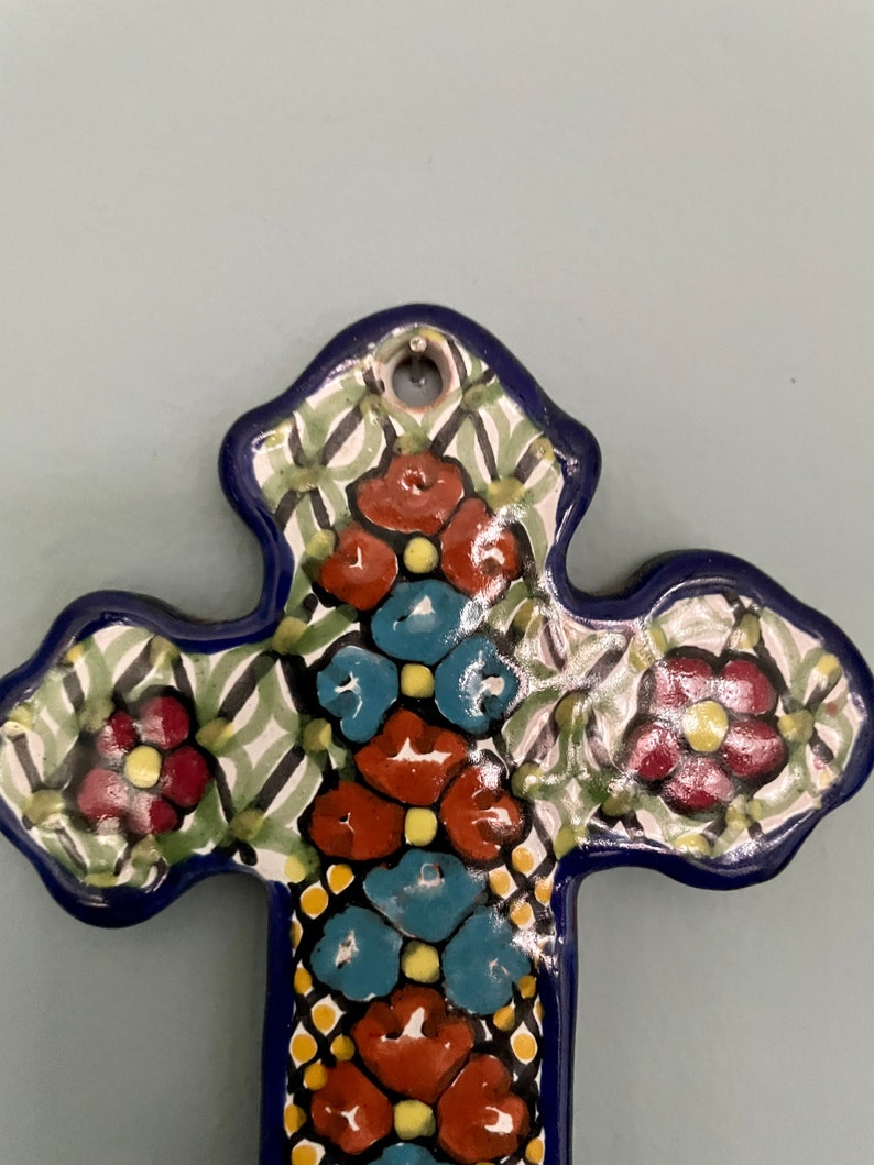 May include: A blue and white ceramic cross with a floral design. The cross is decorated with red, blue, and yellow flowers.