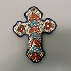 May include: A ceramic cross with a blue border and intricate floral designs in shades of red, green, blue, and yellow.