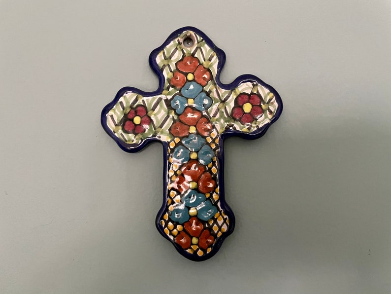 May include: A ceramic cross with a blue border and intricate floral designs in shades of red, green, blue, and yellow.