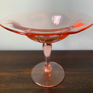 May include: A pink glass pedestal bowl with a scalloped edge and a fluted stem.