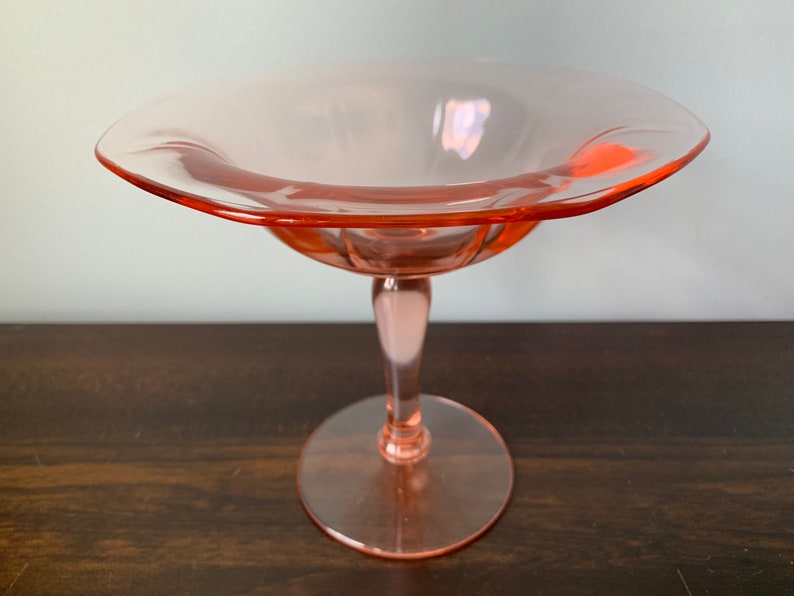 May include: A pink glass pedestal bowl with a scalloped edge and a fluted stem.